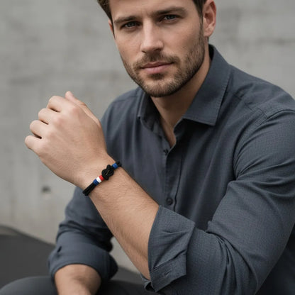 Homem com camisa cinza usando pulseira masculina de corda preta com nó e detalhes em azul, branco e vermelho.