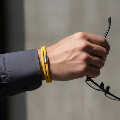Homem segurando um óculos enquanto usa pulseira masculina de corda amarela com volta dupla e fecho metálico prateado.