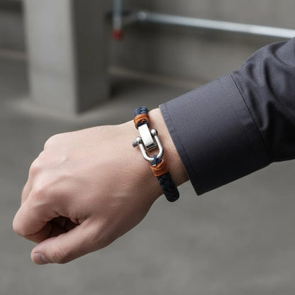 Close no pulso com pulseira masculina de corda azul com detalhes laranja e fecho metálico prateado em fundo neutro.