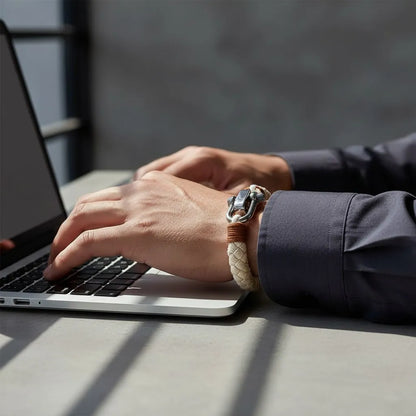 Homem digitando no notebook enquanto usa pulseira masculina de corda bege com detalhes marrons e fecho metálico prateado.