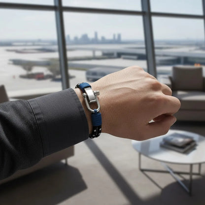 Pulseira masculina de corda preta com detalhes azuis e fecho metálico em destaque no pulso, em ambiente sofisticado com vista panorâmica.