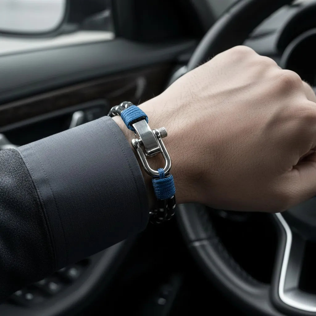 Close da pulseira masculina de corda preta com detalhes azuis e fecho metálico no pulso, dentro de um carro.