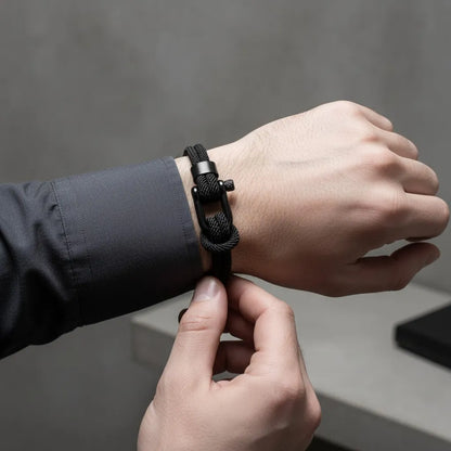 Close no pulso com pulseira masculina de corda preta e fecho preto sendo ajustada com a outra mão.