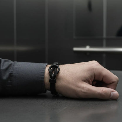 Pulseira masculina de corda preta com design minimalista no pulso de homem em ambiente corporativo.
