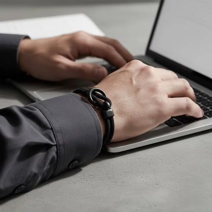 Close da pulseira masculina de corda preta com acabamento fosco no pulso de homem usando notebook.