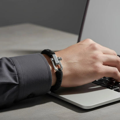 Homem digitando no notebook enquanto usa pulseira masculina de corda preta com fecho metálico prateado.