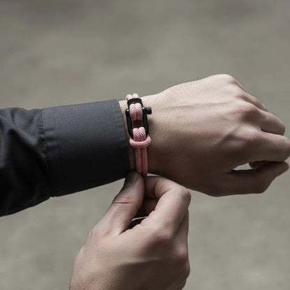 Homem ajustando a pulseira masculina de corda rosa com fecho preto no pulso em close.