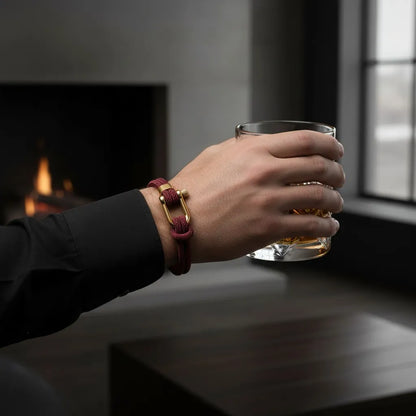 Homem segurando um copo enquanto usa pulseira masculina de corda vinho com design elegante e fecho dourado.