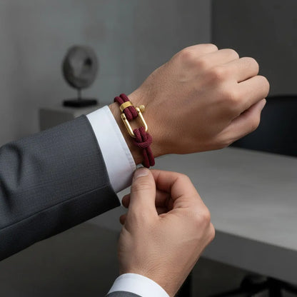 Homem ajustando pulseira masculina de corda vinho com acabamento metálico dourado no pulso.