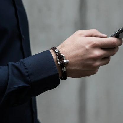 Close do pulso masculino com pulseira de couro marrom e fecho metálico enquanto segura um celular.