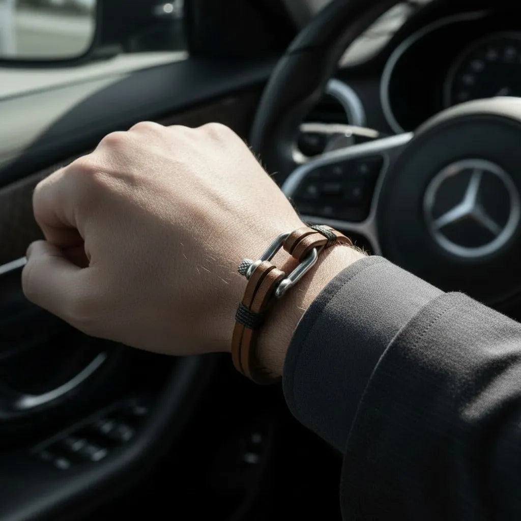Pulseira masculina de couro marrom com acabamento metálico prateado sendo usada no pulso dentro do carro.
