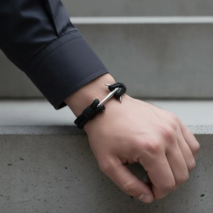 Close da pulseira masculina de couro trançado preto com design moderno e âncora metálica prateada no pulso.