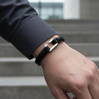Close da pulseira masculina de couro preto com design trançado e acabamento metálico prateado no pulso.
