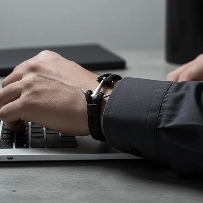 Homem trabalhando no notebook enquanto usa pulseira masculina de couro trançado preto com âncora metálica prateada.