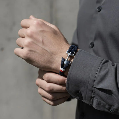 Pulseira de corda azul com âncora em aço no pulso enquanto a outra mão ajusta a manga da camisa.
