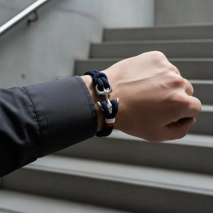Close do pulso usando pulseira de corda azul com âncora em aço, com escadas ao fundo.