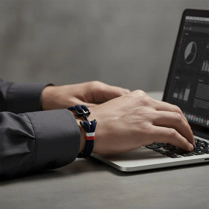 Pulso masculino usando pulseira de corda azul-marinho com detalhe metálico escuro, enquanto digita no notebook.