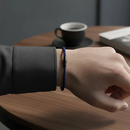 Pulseira masculina de corda azul fina com fecho preto, usada em ambiente casual com mesa e café.