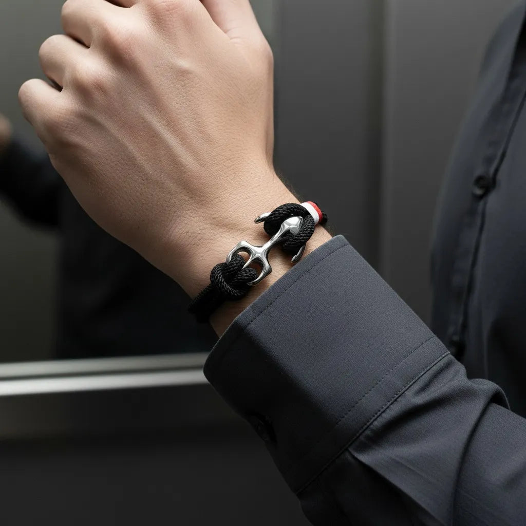 Pulseira de corda preta com âncora em aço no pulso em frente a uma superfície espelhada.