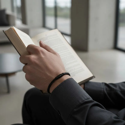 Homem lendo um livro enquanto usa pulseira masculina de corda preta com fecho metálico minimalista.