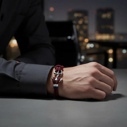 Pulso masculino com pulseira de corda vinho e detalhe metálico prateado em destaque, com cenário urbano noturno desfocado ao fundo.