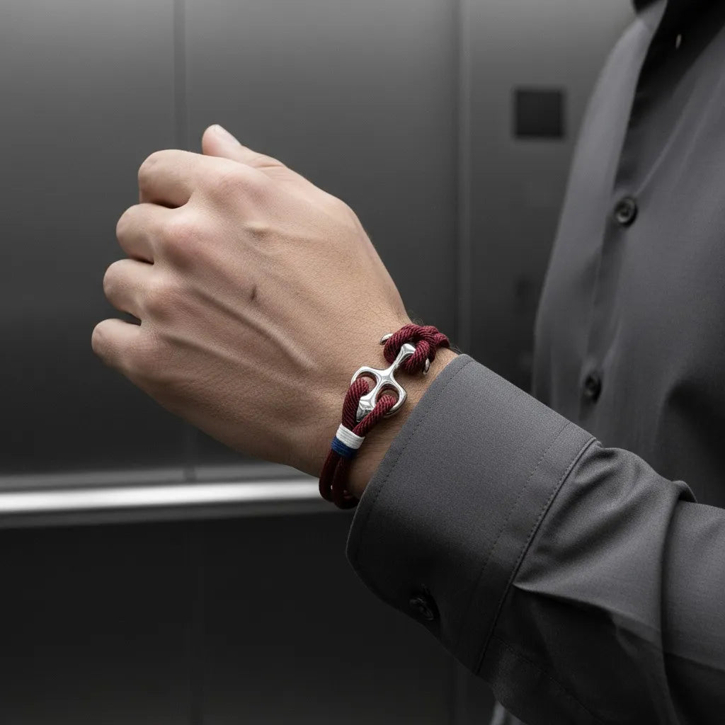 Pulso masculino usando pulseira de corda vinho com detalhe metálico prateado, fotografado dentro de um elevador.