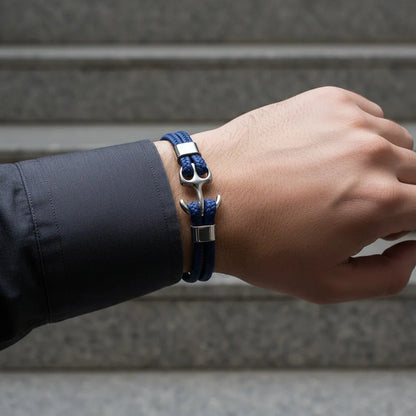 Close da pulseira de couro azul com âncora em metal prateado no pulso, com fundo de escada desfocado.