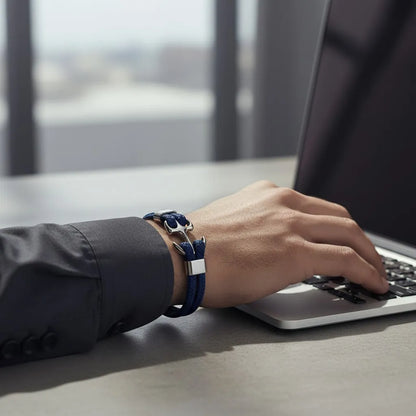 Pulseira de couro azul com âncora em metal prateado no pulso masculino enquanto usa um notebook sobre mesa clara.