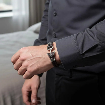 Homem usando pulseira de couro marrom com âncora em metal prateado, combinada com camisa social escura em ambiente interno elegante.