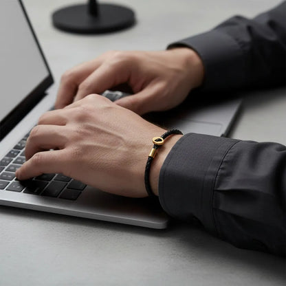 Pulseira de couro preta com detalhes dourados usada no pulso enquanto a pessoa digita em um notebook.