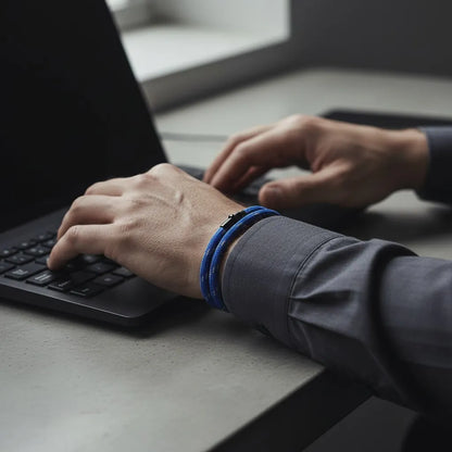 Homem trabalhando no notebook com pulseira masculina de corda azul e acabamento metálico preto.