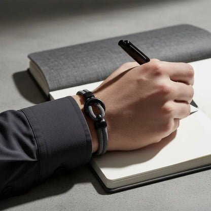 Pulseira masculina de corda cinza com detalhe metálico preto no pulso de homem escrevendo em um caderno.