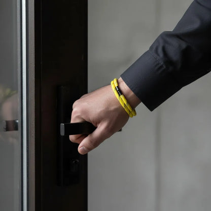 Homem abrindo uma porta enquanto usa pulseira masculina de corda amarela com volta dupla e fecho preto.