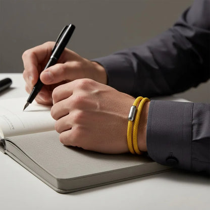Homem escrevendo em um caderno enquanto usa pulseira masculina de corda amarela com volta dupla e fecho metálico prateado.