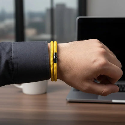 Pulseira masculina de corda amarela de volta dupla no pulso ao lado de um notebook.