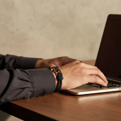 Homem trabalhando no notebook enquanto usa pulseira masculina de corda azul com fecho dourado.