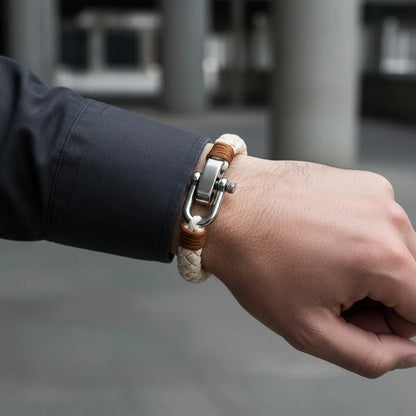 Close no pulso com pulseira masculina de corda bege, detalhes marrons e fecho metálico prateado em fundo neutro.