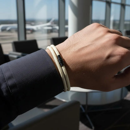 Homem usando pulseira masculina de corda branca com fecho preto em um aeroporto.