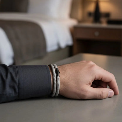 Detalhe de pulseira masculina de corda cinza com fecho preto em ambiente de hotel.
