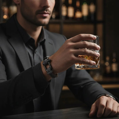Homem com roupa social escura usando pulseira masculina de corda cinza com fecho preto enquanto segura um copo.