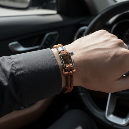 Detalhe de pulseira masculina de corda marrom com fecho metálico prateado dentro de um carro.