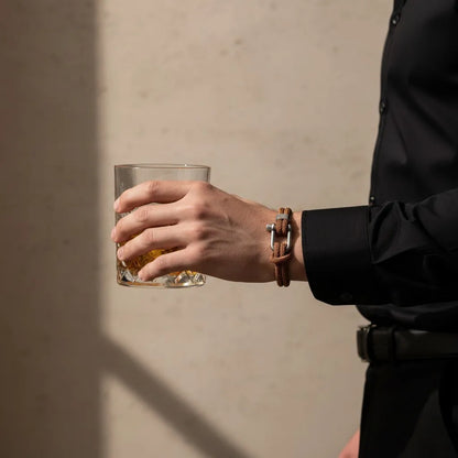 Homem segurando um copo e usando pulseira masculina de corda marrom com fecho prateado.