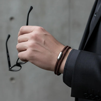 Homem segurando um óculos enquanto usa pulseira masculina de corda marrom com volta dupla e fecho metálico prateado.