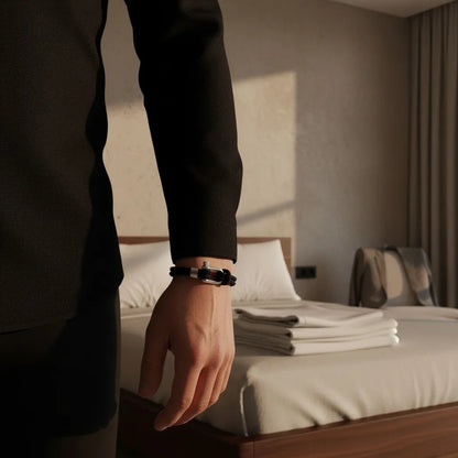 Homem usando pulseira masculina de corda preta com fecho metálico em um quarto de hotel.