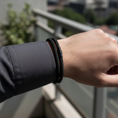 Pulseira masculina de corda preta no pulso de um homem em área externa.