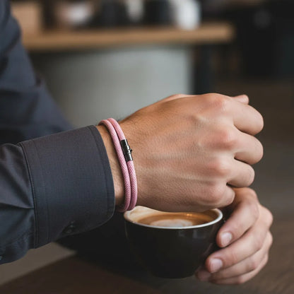 Homem segurando uma xícara de café e usando pulseira masculina de corda rosa com fecho preto.