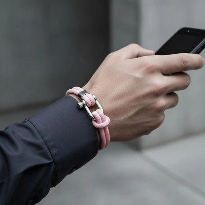 Homem usando celular e pulseira masculina de corda rosa com fecho metálico prateado.