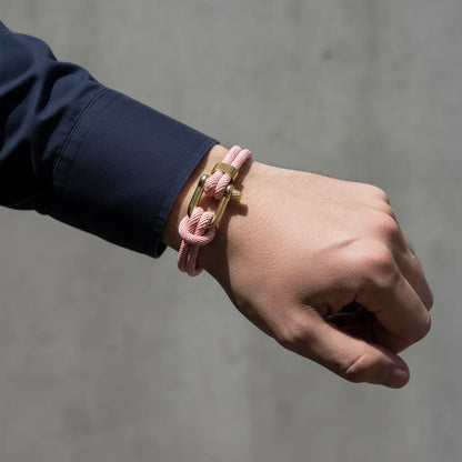 Close da pulseira masculina de corda rosa com fecho dourado no pulso, em um fundo minimalista cinza.