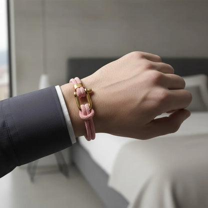 Homem usando pulseira masculina de corda rosa com fecho dourado em um ambiente elegante de quarto.