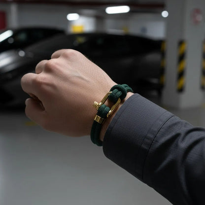 Homem usando pulseira masculina de corda verde com acabamento dourado em um ambiente moderno de estacionamento.